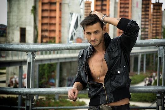 Handsome man outdoor in urban environment wearing leather jacket on naked torso