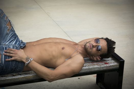 Handsome shirtless man outdoor resting on bench, looking at camera
