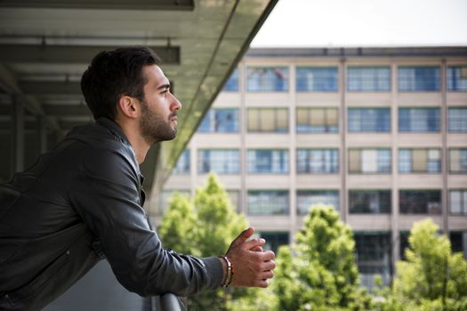 Profile  shot of attractive bearded young man in city, looking afar outdoors