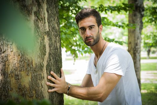 Handsome young man leaning against tree as if he were pushing it