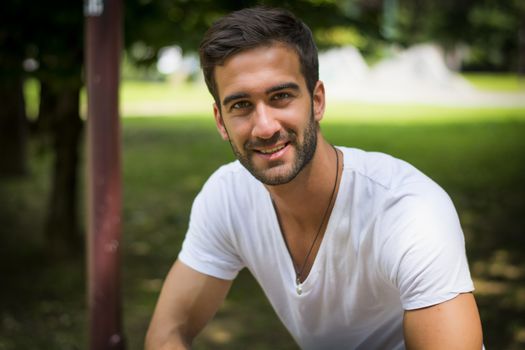 Handsome friendly young man outdoors in park smiling at camera