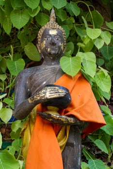 Thai monk statue in temple holding alms bowl, with Bo leaves around