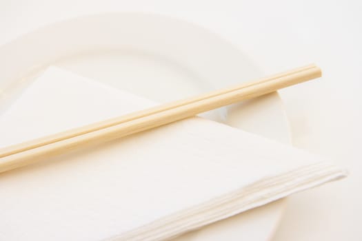 Closeup view of wooden chopsticks on white plate with paper napkin, shallow depth of field