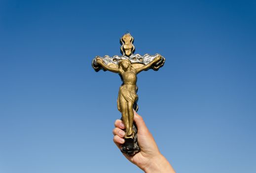 symbol of christianity metal cross with the crucified christ in woman hand on blue sky background