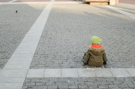 lonely child with thick jacket sit on the pavement in old town