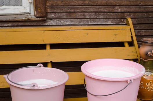 two pink plastic pail full of fresh cow milk on wooden bench