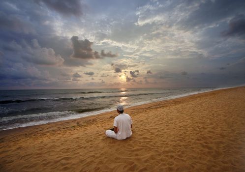 Guy meditating at sunset sitting on coastline. Sri Lanka