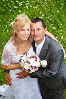 beautiful young wedding couple, blonde bride with flower and her groom against green grass, view from top