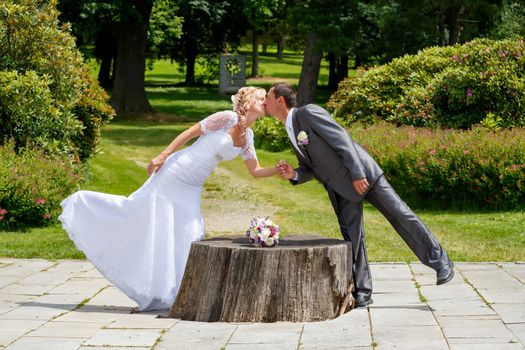 beautiful young wedding couple, blonde bride kissing her groom outdoor