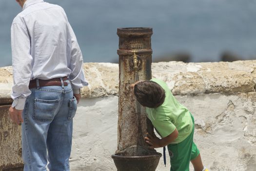 A child drinks water from an old fountain in the old town of Gallipoli (Le) in the southern of Italy