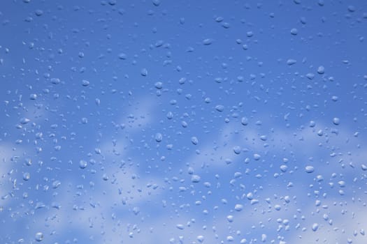 rain drops on window pane and blue sky with white clouds