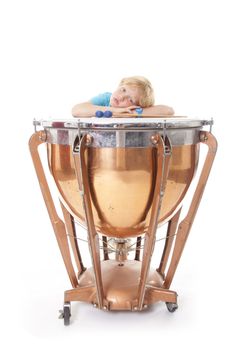 young boy resting his arms on kettle drum against white background in studio