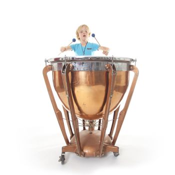 young boy playing kettle drum against white background in studio