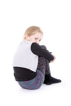 young girl sitting in studio against white background with sorrowful expression