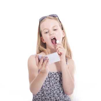 young blond girl applying lipstick in studio against white background