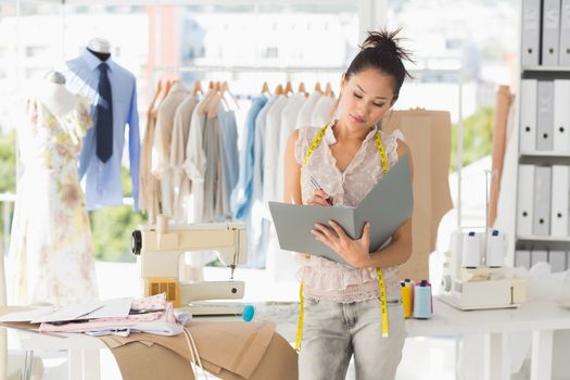 Beautiful female fashion designer looking at folder in the studio