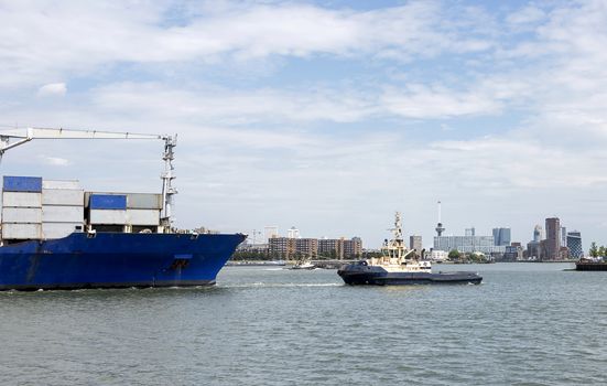 containership entering rotterdam harbor with tug and skyline as background