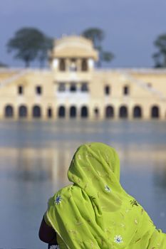 Indian lady in colorful sari looking out over the Water Palace (Jal Mahal) in the middle of Man Sagar lake. Jaipur, Rajasthan, India. 18th Century