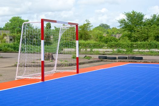 Side of red and white goal and blue and orange soccer field.