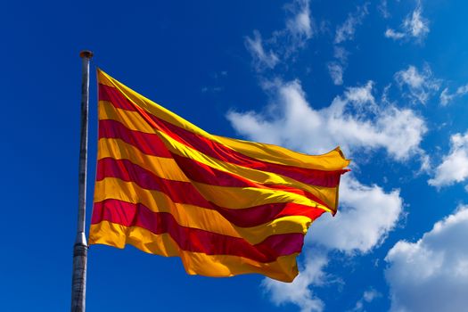Catalan flag with pole blowing in the wind on blue sky with clouds