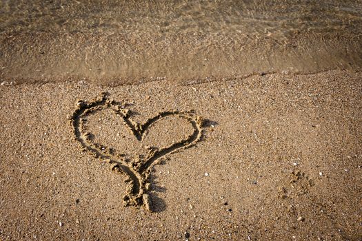 drawing of a heart on sandy beach with water