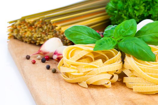 Italian pasta fettuccine nest with garlic and fresh basil leaves, on wooden board