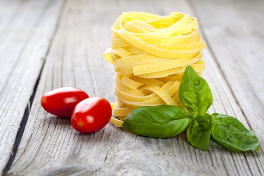 Italian pasta fettuccine nest with tomatoes and fresh basil leaves, on wooden background