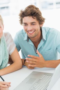 Closeup of a smiling young man with laptop at desk in a bright office