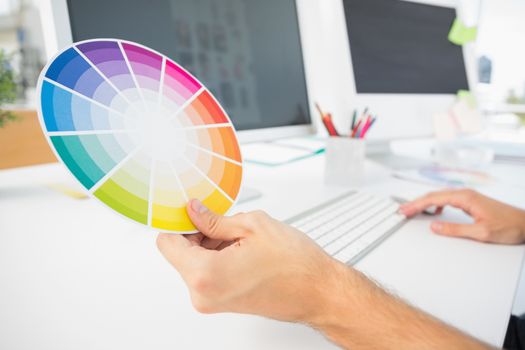 Closeup of hand holding color wheel while using computer at desk