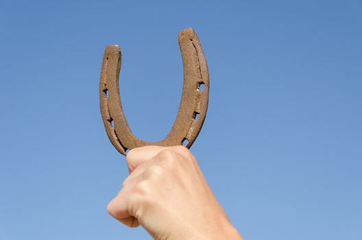 female hand hold old rusty iron horseshoe on blue sky background, symbol of luck happiness