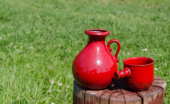 close up of two ceramic red water jug and cup on stump nature background