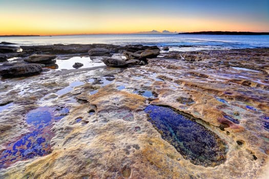 Beautiful sunrise, a clear morning on the rocks at Cronulla NSW Australia with colourful rocks and rockpools in foreground.