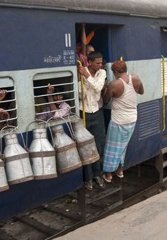 Hanging onto the doorway of a moving train. Milk churns hanging from the windows. Delhi, India.