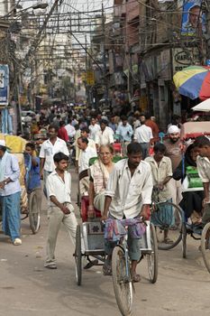 Man negotiating a cycle rickshaw through a crowded street in Old Delhi India.