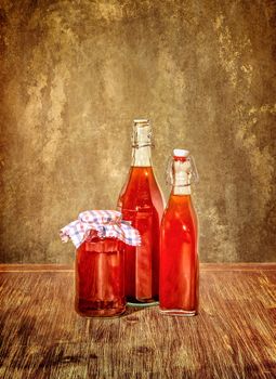 Bottles filled with yellow syrup and jam on kitchen table in vintage filtered style