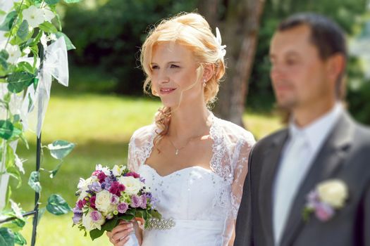 beautiful young couple in wedding ceremony outdoor, blonde bride with flower and groom, focus to bride