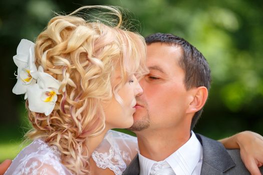 beautiful young wedding couple, blonde bride kissing her groom outdoor