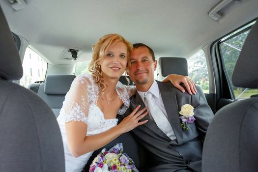 beautiful young wedding couple, blonde bride with flower and her groom in car, wide shoot