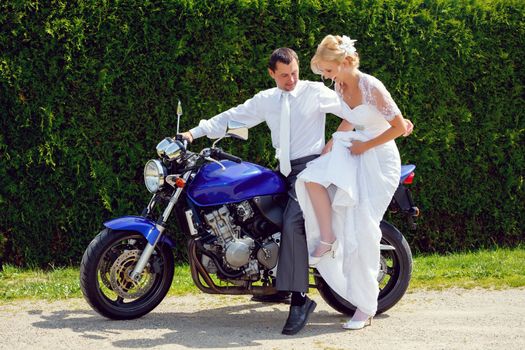 beautiful young wedding couple, blonde bride with flower try sit to motorcycle with her groom
