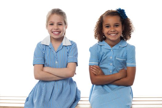 Smiling school girls sitting in bench, arms folded