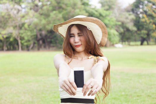 Woman handing the smart phone standing on the grass in the park.