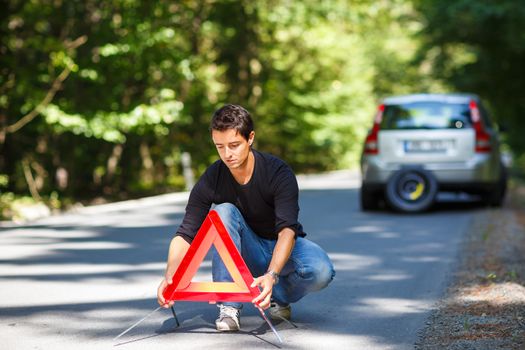 Handsome young man with his car broken down by the roadside, setting the safety triangle