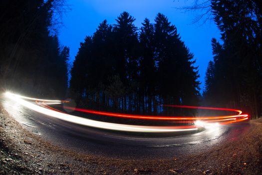 Cars going fast through a curve on a forest road at dusk, on a rainy day - i.e. Potentially dangerous driving conditions