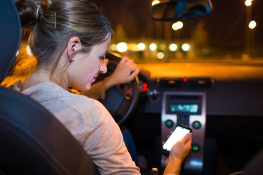 Pretty young woman using her smart phone while driving her car at night