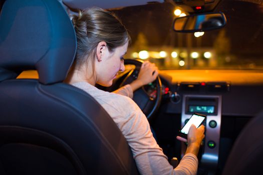 Pretty young woman using her smart phone while driving her car at night