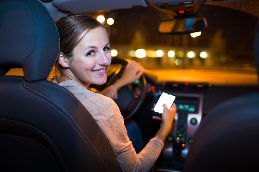 Pretty young woman using her smart phone while driving her car at night