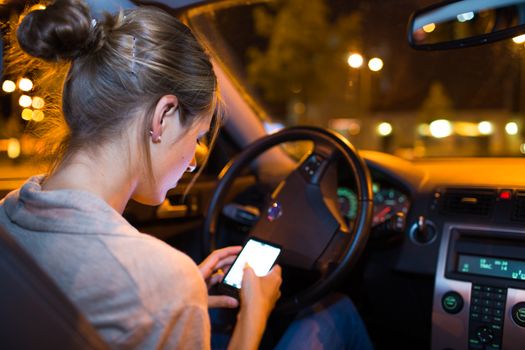 Pretty young woman using her smart phone while driving her car at night