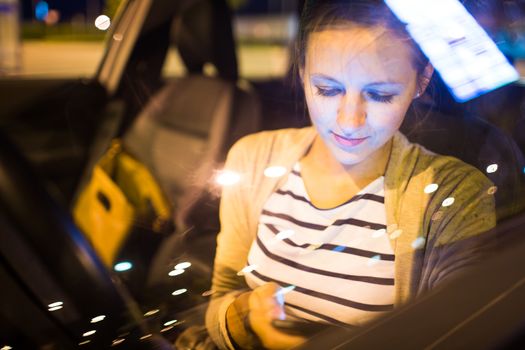 Pretty young woman using her smart phone while driving her car at night