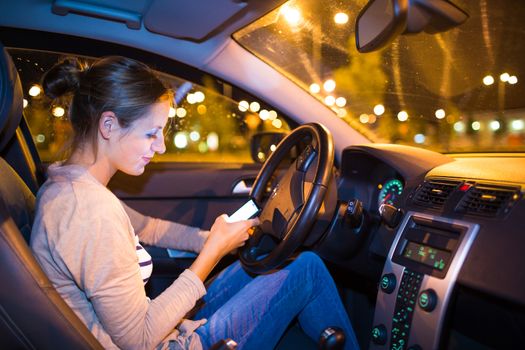 Pretty young woman using her smart phone while driving her car at night