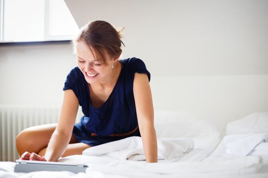 Elegant, smart, young woman using her tablet computer in bed (shallow DOF; color toned image)